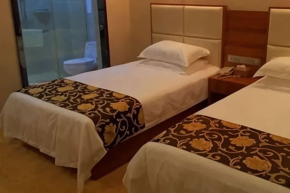 Habitación de hotel con dos camas, cabina de ducha de vidrio y cabecera de madera.