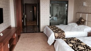 Een hotelkamer met twee bedden, een televisie, een sofa en een zichtbare badkamer door een glazen deur.