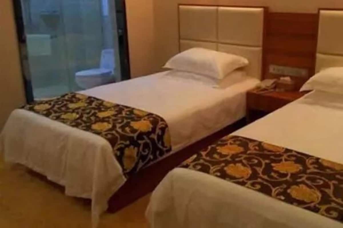 Une chambre d’hôtel avec deux lits, une tête de lit en bois et une table de chevet avec une lampe.