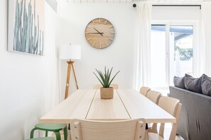Enjoy meals in this dining area with a wooden table and chairs, a round wall clock, and a potted plant.