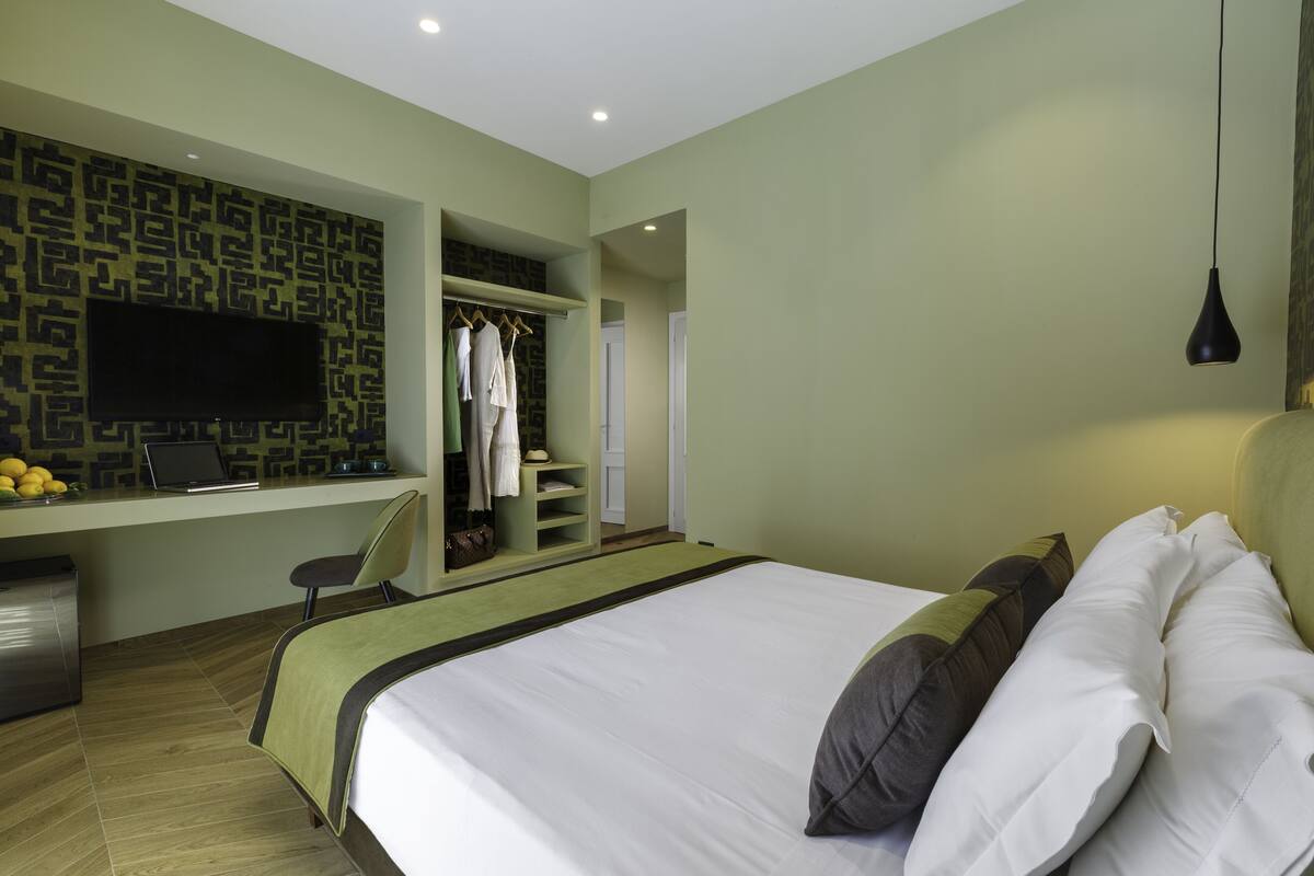 A bedroom with a bed, a desk with a laptop, a TV, and a wardrobe.