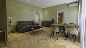 A modern living room with a sofa, coffee table, and dining area with chairs. - Dreamers' Rooms Sorrento (Sorrento)