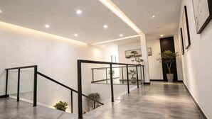 A modern interior with a glass railing staircase, recessed ceiling lights, and framed artwork on the walls.
