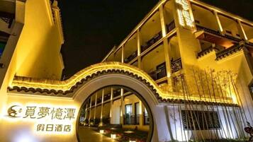 A hotel entrance with a large arched gateway, illuminated signage, and a pathway leading to the building.
