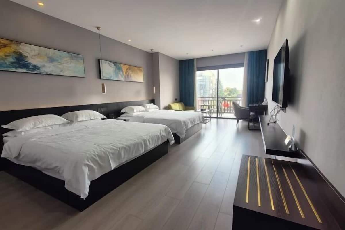 A hotel room with two beds, a desk, a TV, and a balcony with a view.