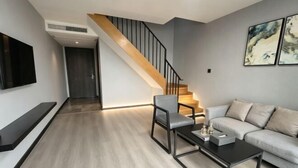 A modern living room with a staircase, a flat-screen TV, a sofa, a coffee table, and artwork on the wall.