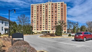 A multi-story hotel with a central entrance, a parking lot, and a red car parked nearby. - Ideally Located Studio w/ Off-Street Parking! (Gadsden)