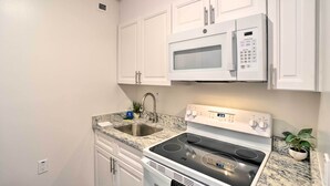 A kitchen with white cabinets, a stainless steel sink, a white stove, and a microwave. - Ideally Located Studio w/ Off-Street Parking! (Gadsden)
