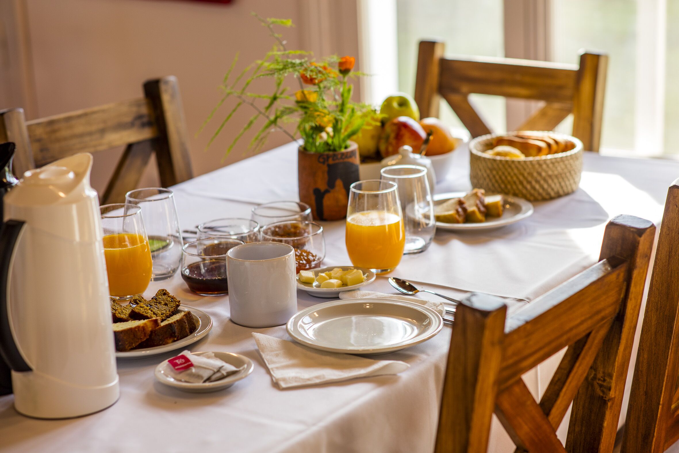 A breakfast table set with plates, glasses, a coffee pot, and a fruit bowl.