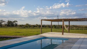 Une piscine dotée d’une pergola et offrant une vue sur un champ verdoyant.