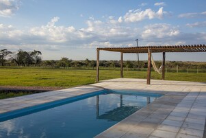 Una piscina con una pérgola y vistas a un campo cubierto de césped.