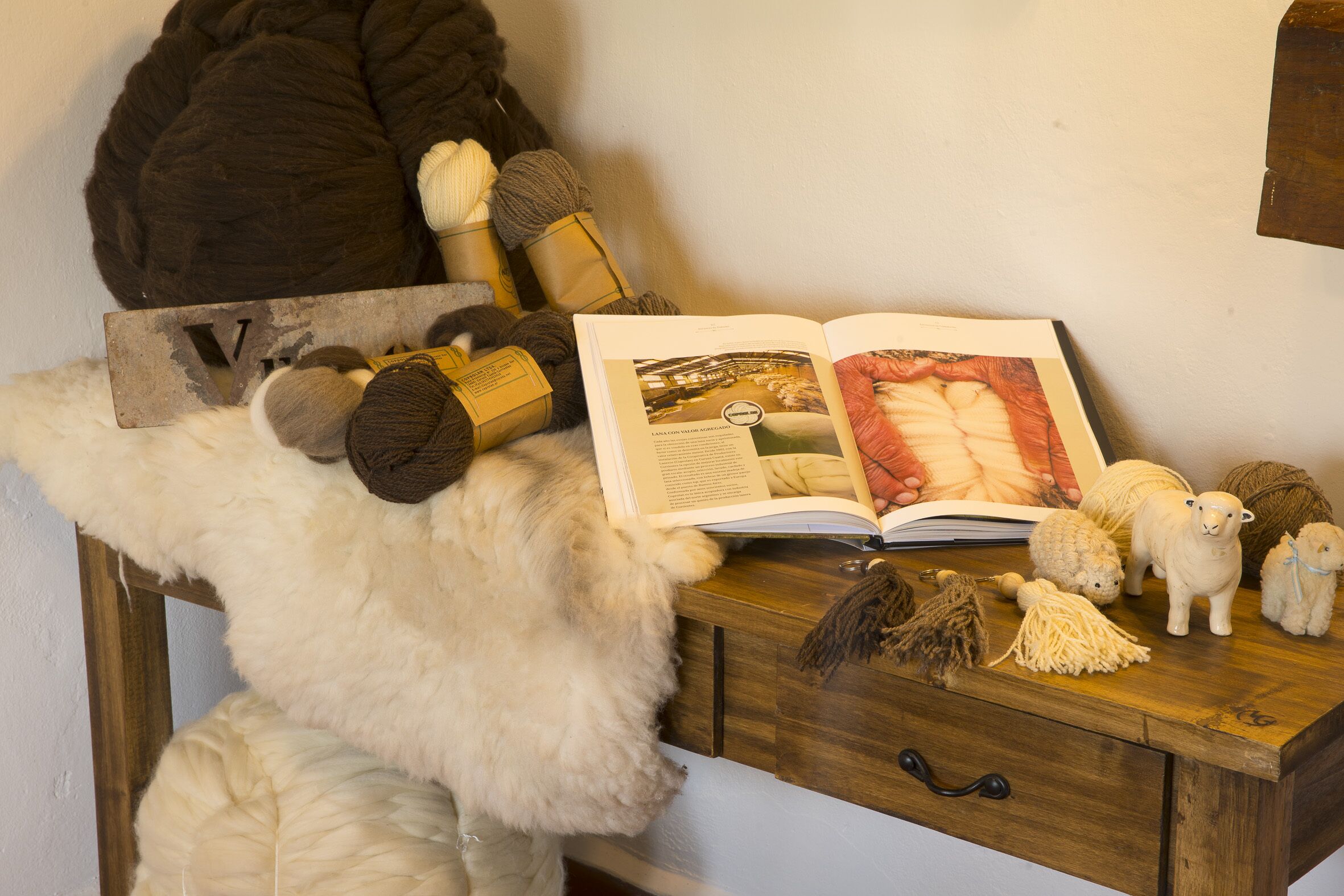 Un escritorio de madera con un libro, lana e impermeable de lana.