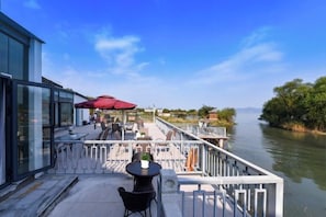 An outdoor deck with tables and chairs, overlooking a calm body of water and greenery. - Juanshui Hostel (Suzhou)
