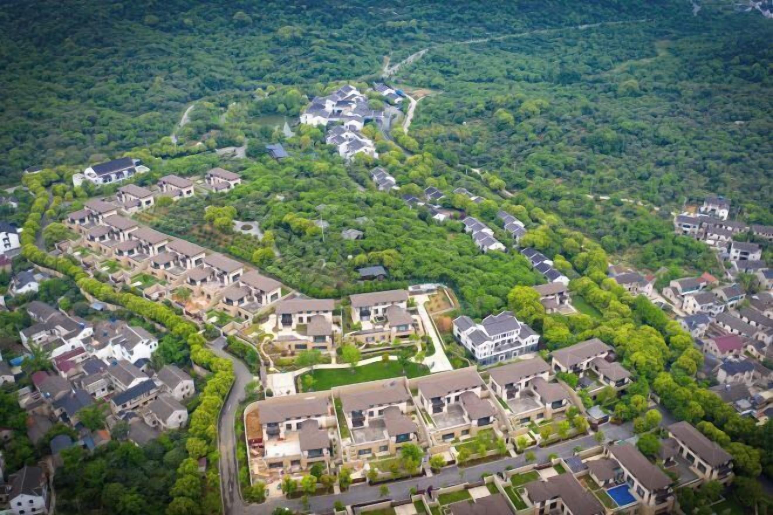 An aerial view of a residential area with houses arranged in a semi-circular pattern, surrounded by dense greenery.