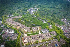An aerial view of a residential area with houses arranged in a semi-circular pattern, surrounded by dense greenery. - Juanshui Hostel (Suzhou)