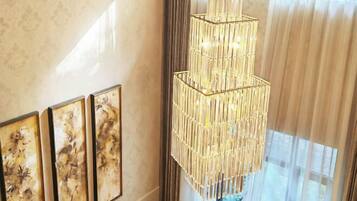 Un lustre au design géométrique est suspendu dans une pièce dotée d’une grande fenêtre et de trois œuvres d’art encadrées accrochées au mur.
