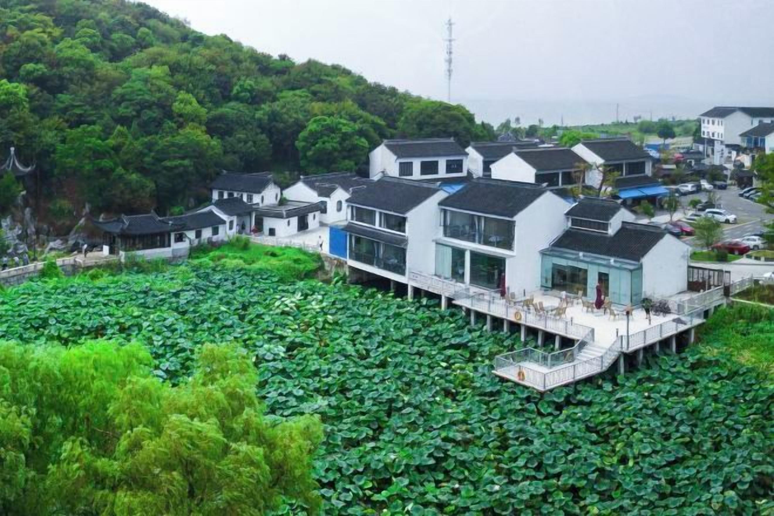 Ein Gebäude im traditionellen Stil mit einem modernen Anbau, das auf Stelzen über einem Gewässer steht, umgeben von üppiger Vegetation.