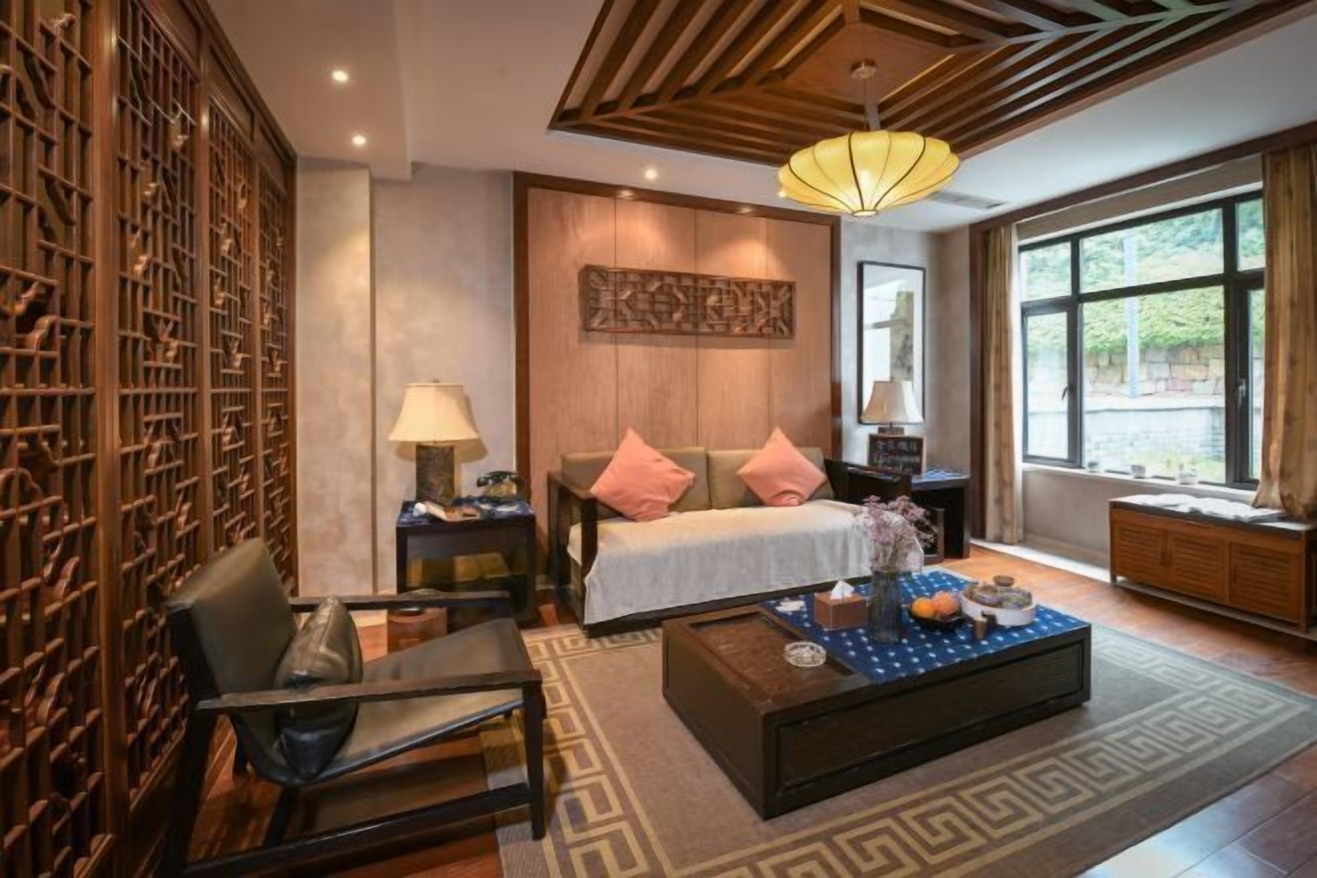 A modern hotel room with a bed, bedside tables, a coffee table, and a large window.