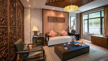 A modern hotel room with a bed, bedside tables, a coffee table, and a large window.