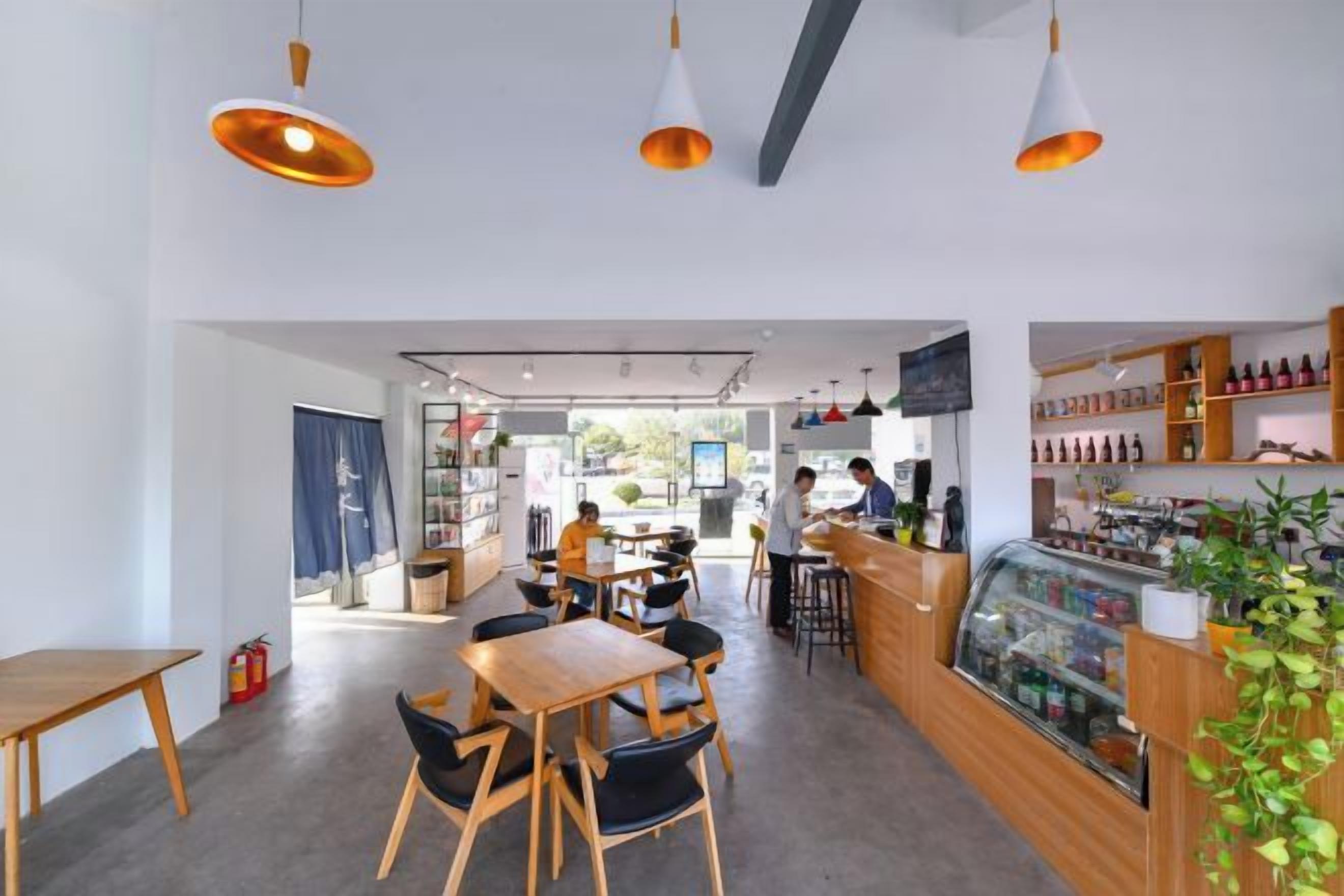 A café interior with wooden tables and chairs, a counter with a display case, and hanging pendant lights.