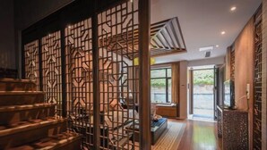 Una scala con un pannello decorativo in legno, una zona giorno con un divano e un tavolino, e vista sull'esterno.