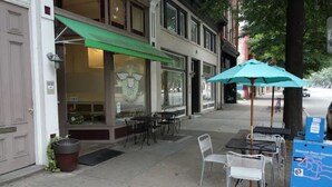 An outdoor seating area with tables and chairs, a green awning, and a blue information box on the sidewalk. - RVA Arts District near VCU MCV (Richmond)