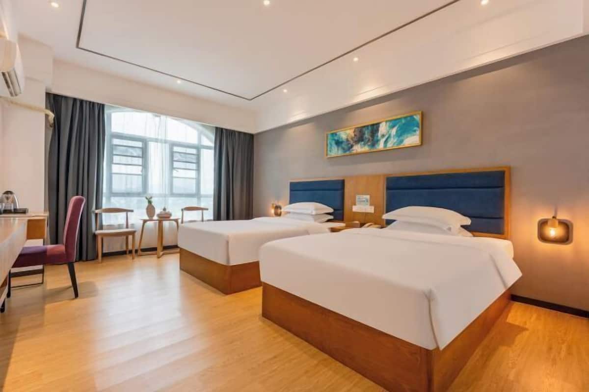 Une chambre d’hôtel avec deux lits, un bureau, une chaise et une fenêtre avec des rideaux.