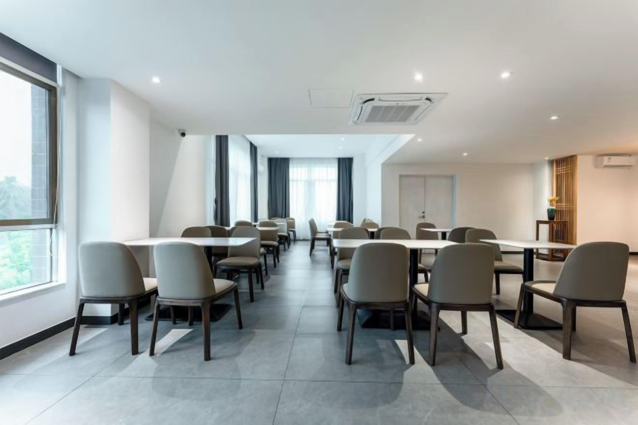 Un salón de conferencias con varias mesas y sillas, ventanas amplias y un diseño moderno.