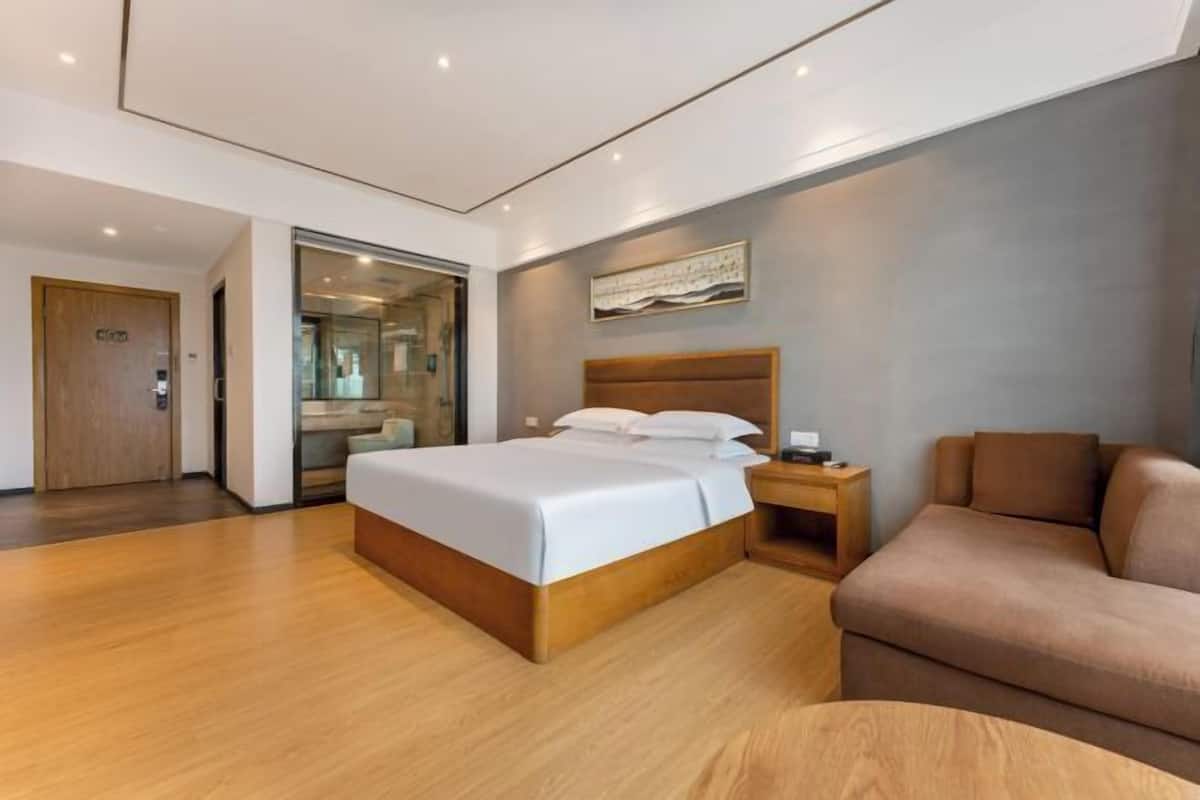 Une chambre d’hôtel moderne avec un lit en bois, une table de chevet, un canapé marron et un grand miroir.