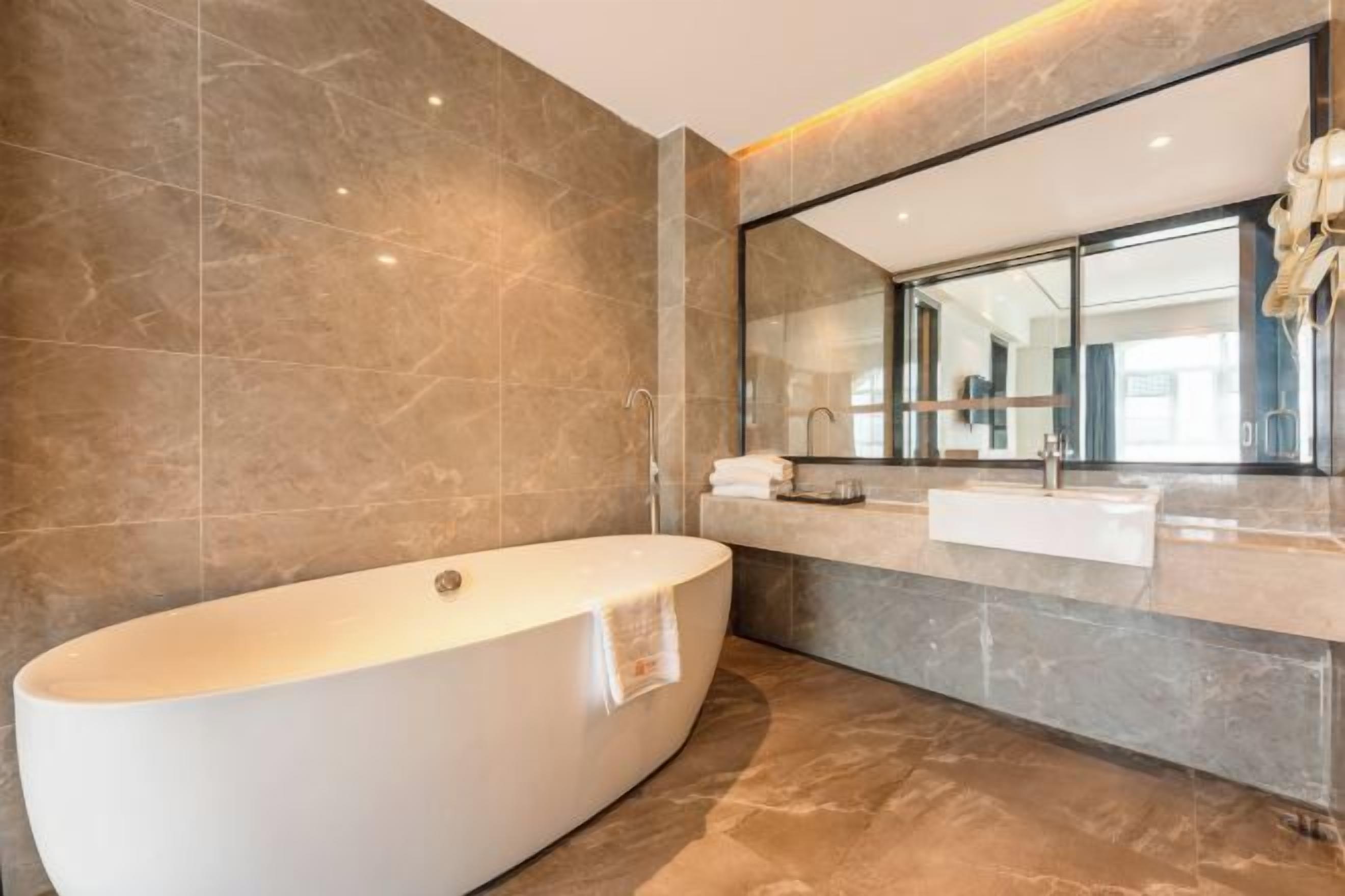 A modern bathroom with a freestanding bathtub, a large mirror, and a marble countertop.