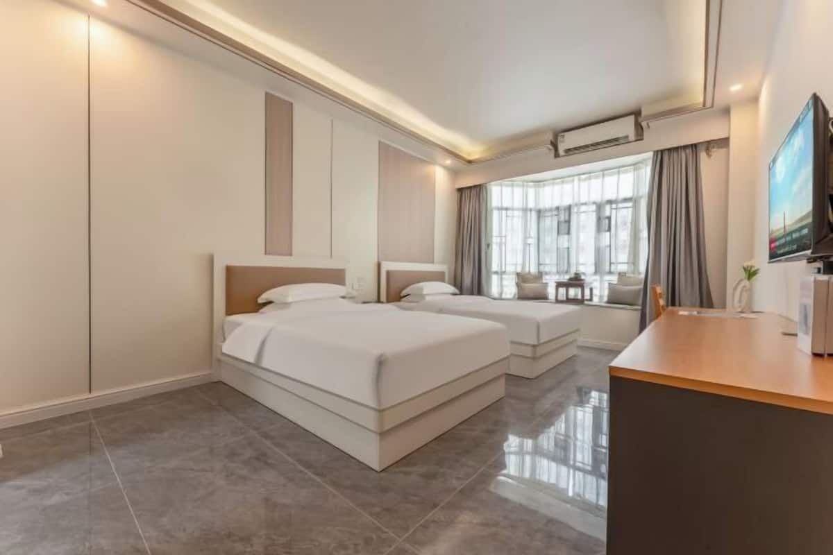 Une chambre d’hôtel moderne avec deux lits, un bureau en bois et une grande fenêtre avec des rideaux.