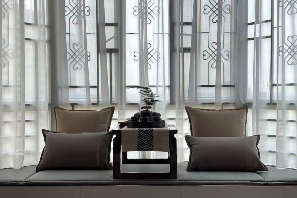 Un coin salon avec un canapé et une petite table, un objet décoratif posé sur la table, et une fenêtre agrémentée d’un rideau à motifs.