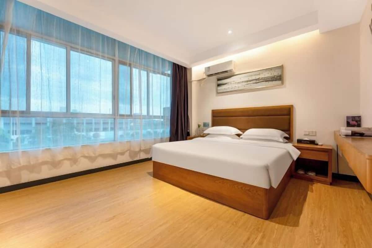 Une chambre d’hôtel moderne dotée d’un grand lit, d’une table de chevet, d’une commode, d’une fenêtre avec des rideaux et d’un appareil de climatisation.