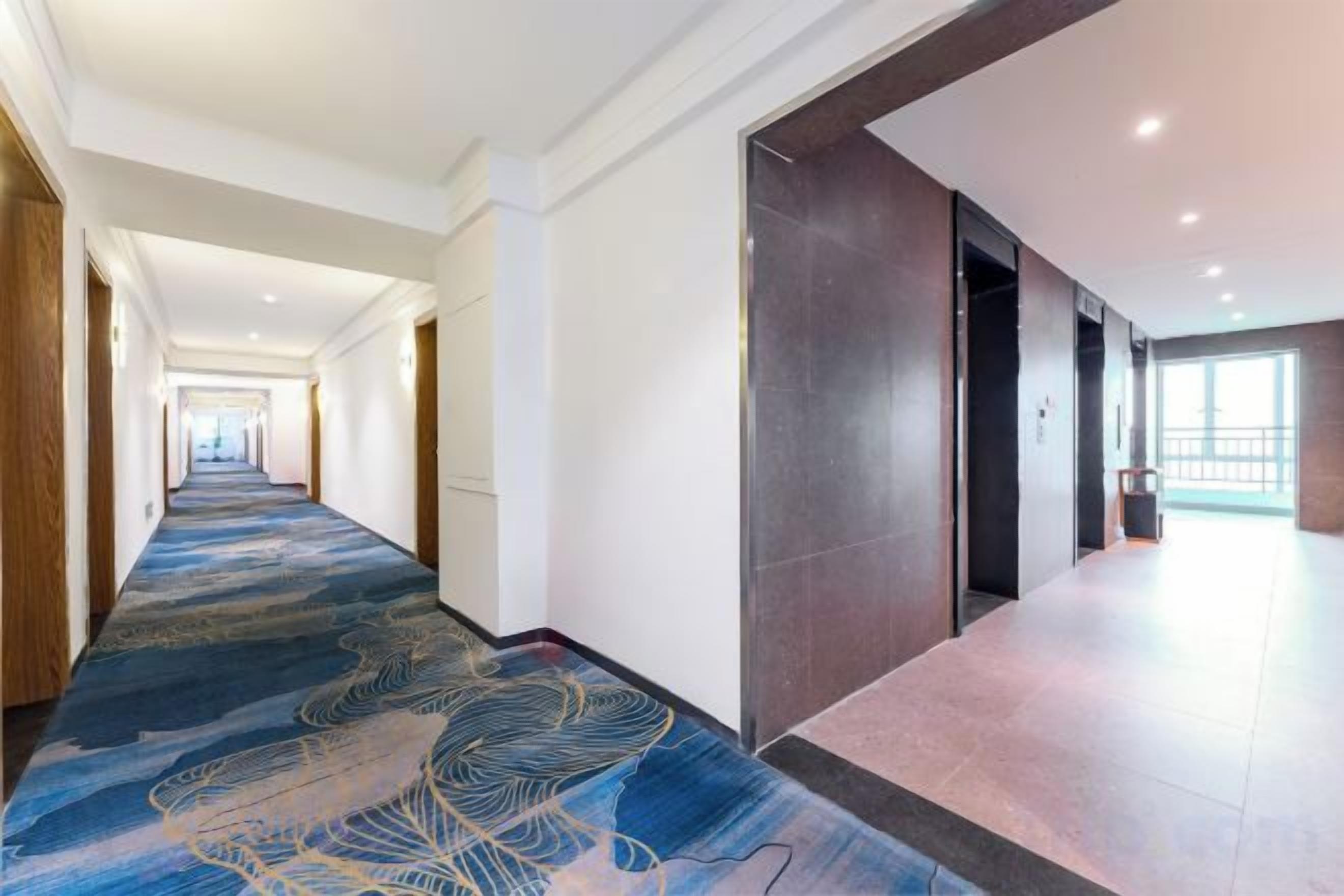 A hotel corridor with a patterned carpet, wooden doors, and a view to the outside.