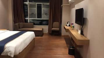 A hotel room with a bed, a sofa, a TV, and a window with curtains.