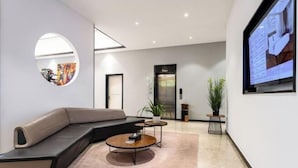 A modern interior with a curved sofa, two small round tables, a large mirror, and a television screen on the wall. - Jiangmen Jinli Hotel (Siqian Town Center Avenue Branch) (Jiangmen)