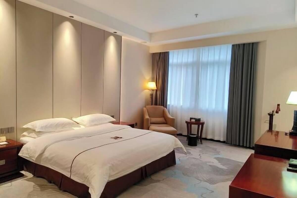 Una habitación de hotel con una cama grande, una silla, un escritorio y un ventanal con cortinas.