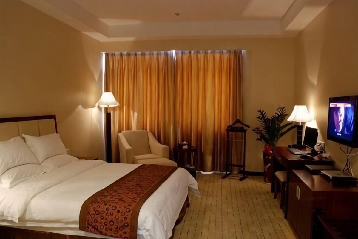 A hotel room with a bed, a desk, a chair, a television, and a window with curtains.