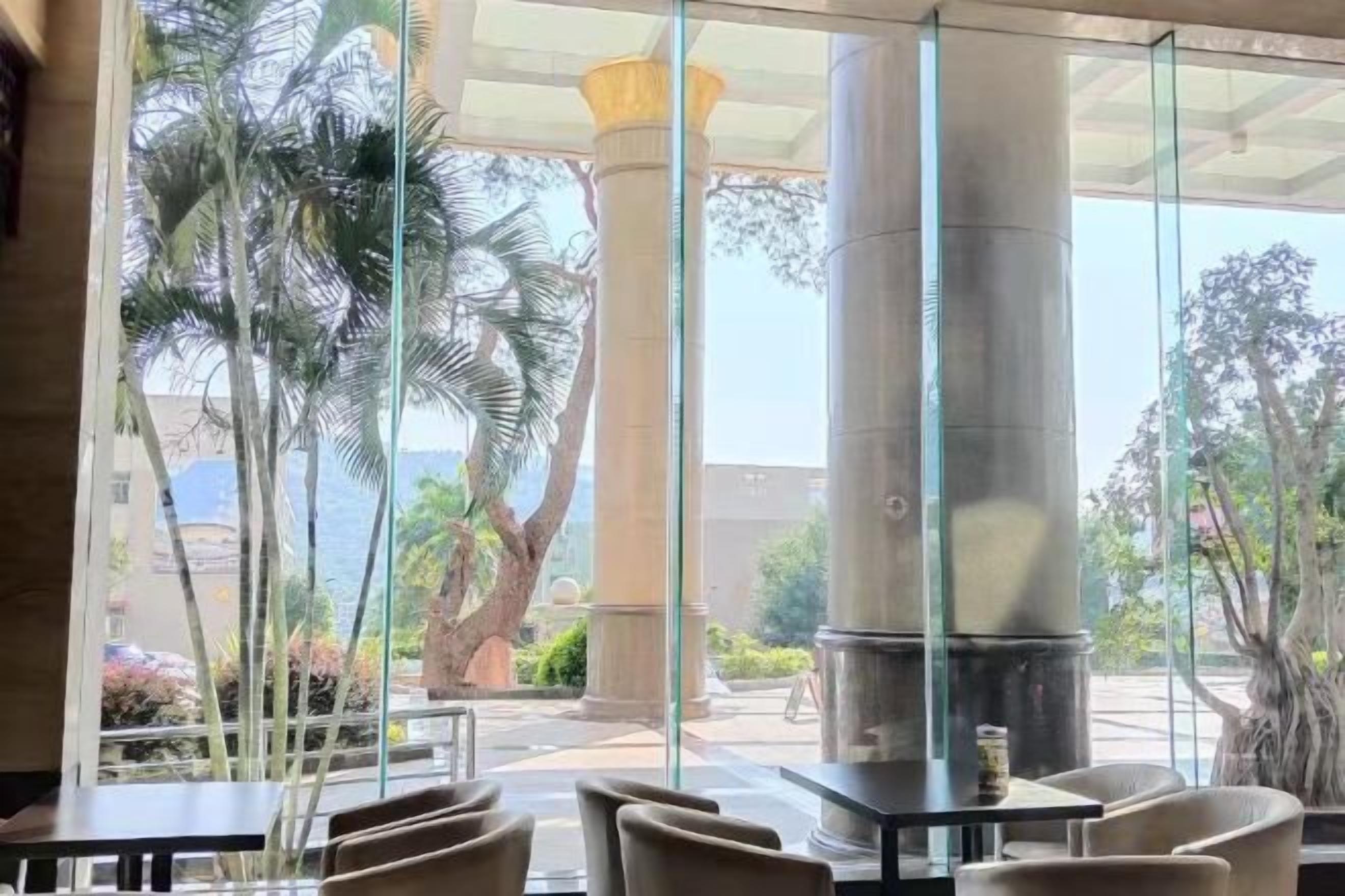Un espace de détente intérieur avec des tables et des chaises, de grandes fenêtres en verre et une vue sur des palmiers et un bâtiment à l’extérieur.