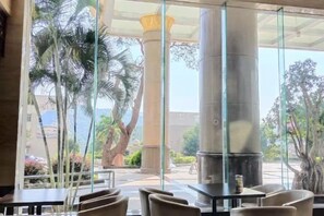 An indoor seating area with tables and chairs, large glass windows, and a view of palm trees and a building outside. - Hua'an Hotel (Hua'an)
