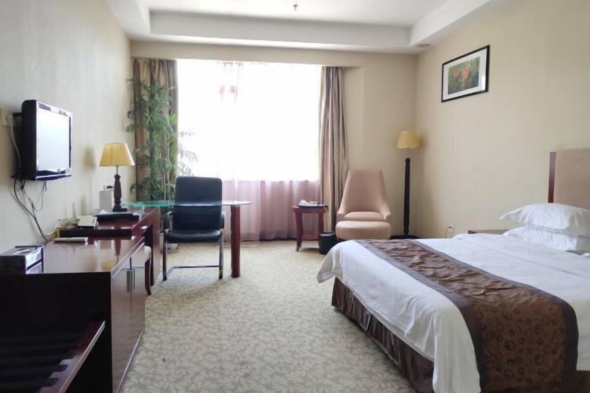 Habitación de hotel con una cama, un escritorio con computadora, una silla, un televisor y una ventana con cortinas.