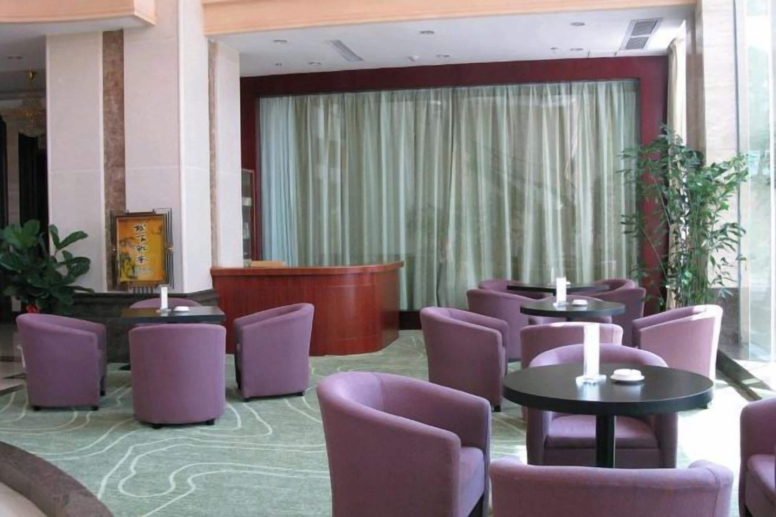 Un hall con sillas y mesas moradas, una recepción y un gran telón.