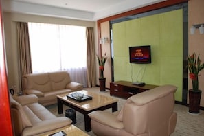 A hotel room with a beige sofa, a coffee table, a TV mounted on a green wall, and two potted plants. - Hua'an Hotel (Hua'an)