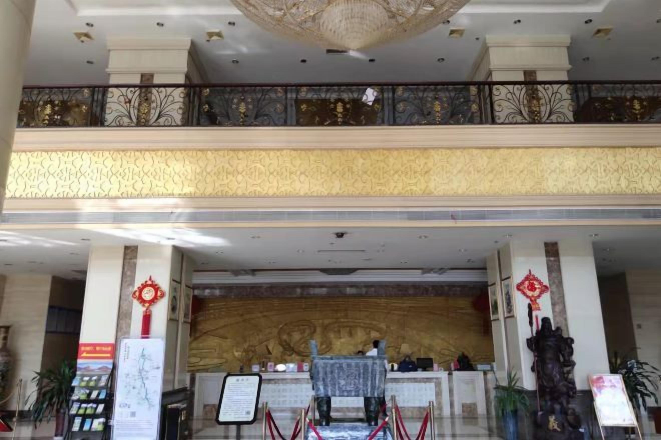 A hotel lobby with a reception desk, a chandelier, and a decorative wall.