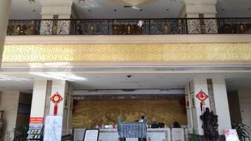 A hotel lobby with a reception desk, a chandelier, and a decorative wall.