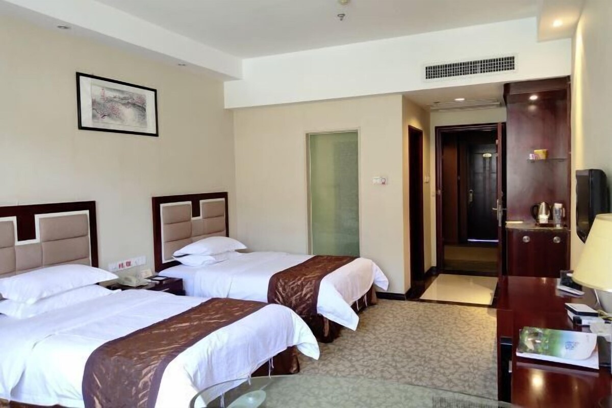 Een hotelkamer met twee bedden, een bureau, een stoel, een televisie en een deur die naar een andere kamer leidt.