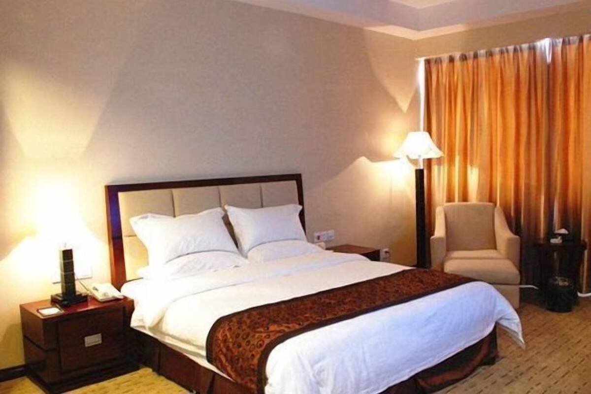 Una habitación de hotel con una cama grande, una silla, una mesita de noche con lámpara y una cortina.