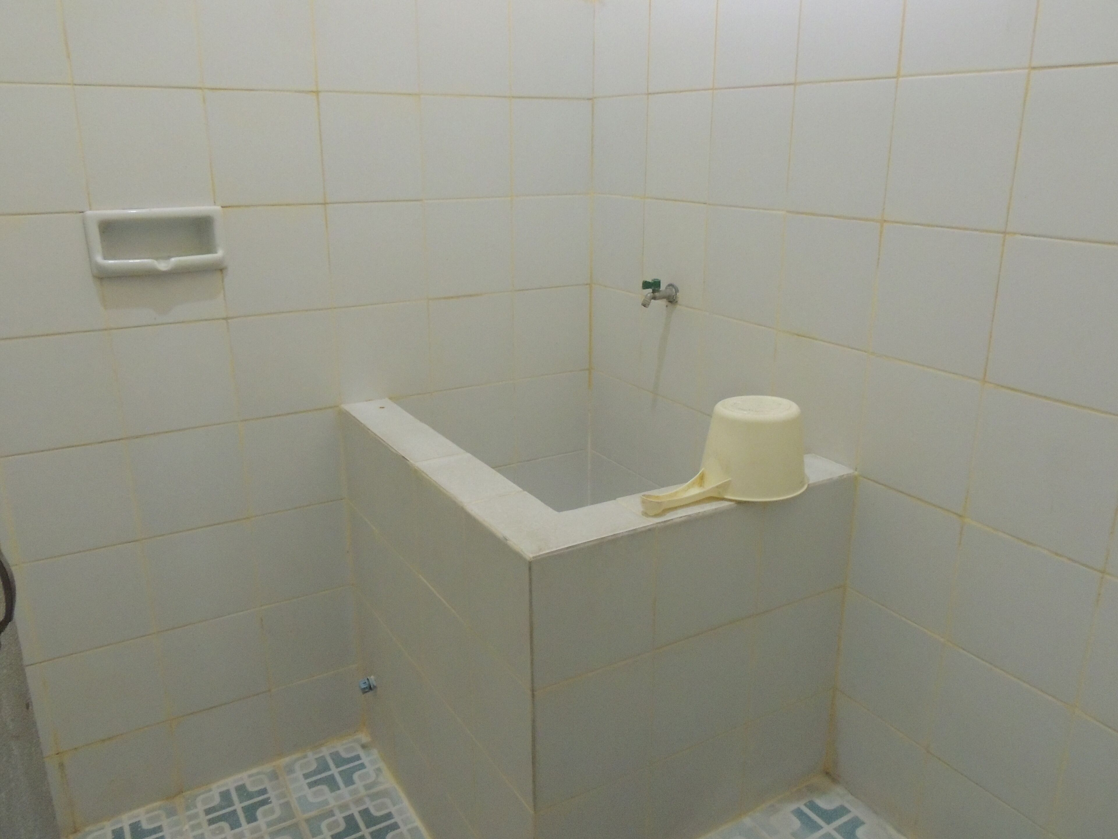 Une petite salle de bain carrelée, équipée de toilettes, d’un lavabo et d’une douche.