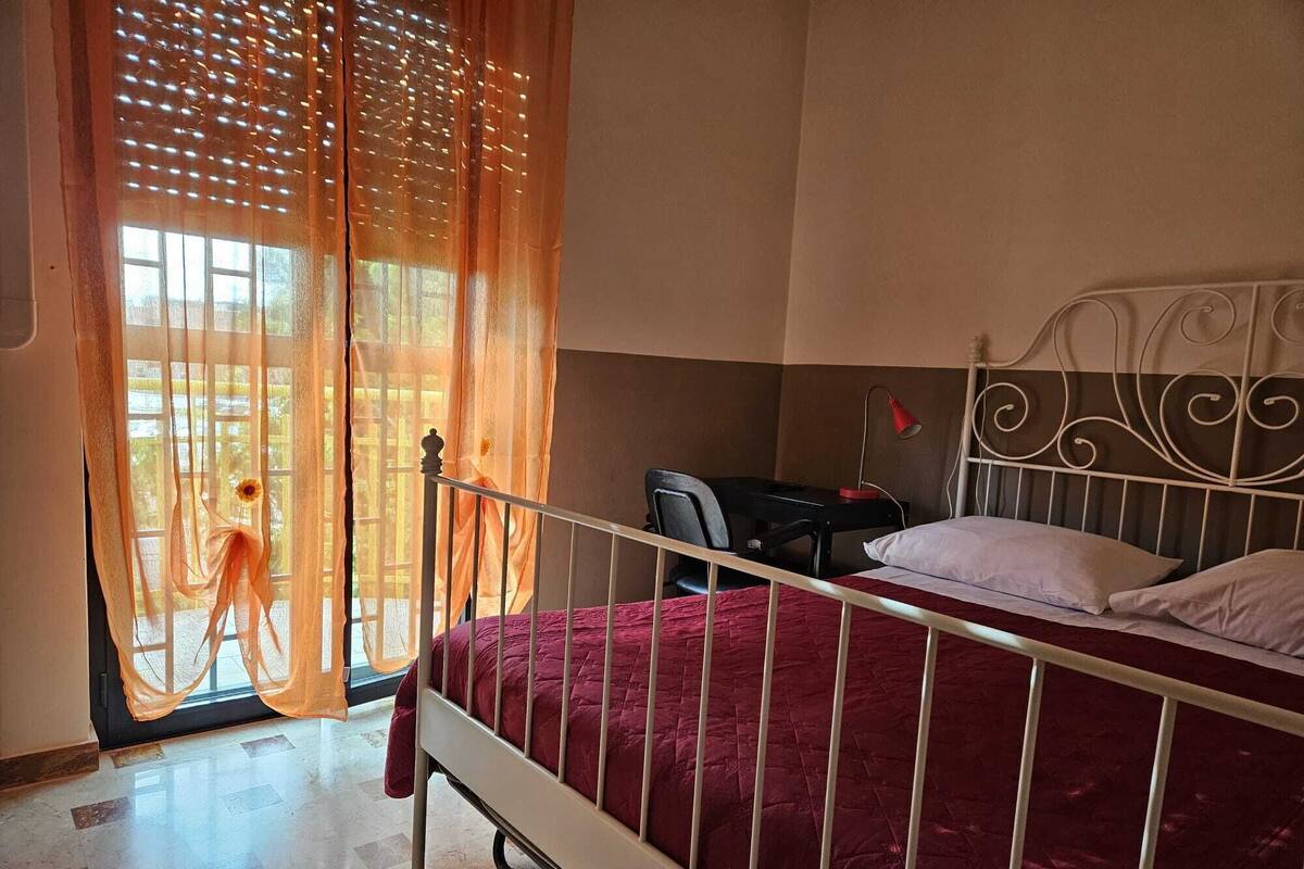 Un dormitorio con cama, escritorio, silla y ventana con cortinas.