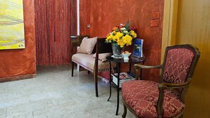 Ein Zimmer mit Holzboden, einem roten Vorhang, einem Holzstuhl, einem Tisch mit Blumenvase und einem Spiegel an der Wand.